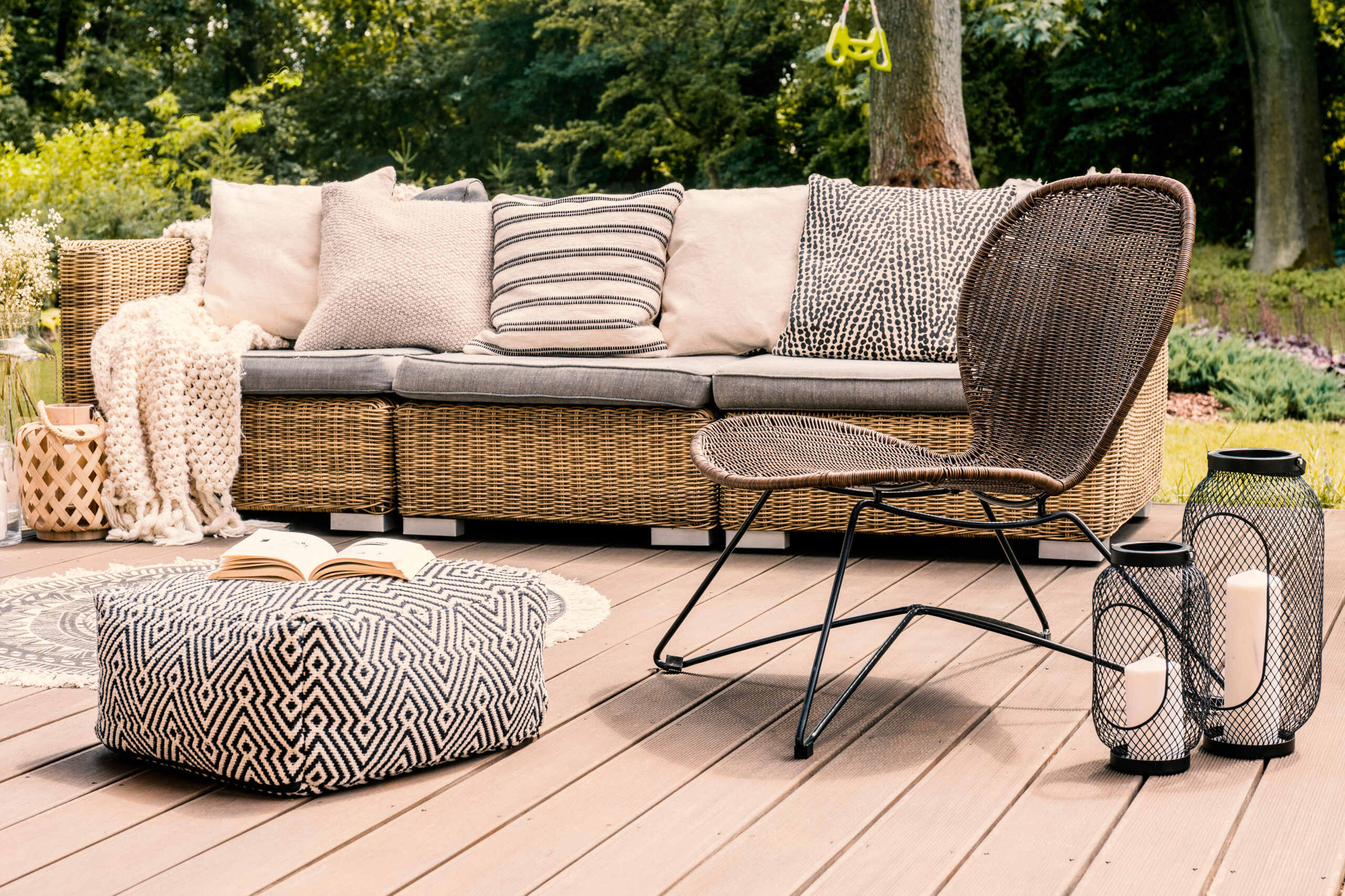 Patterned pouf and rattan chair on wooden patio with pillows on sofa and lanterns. Real photo